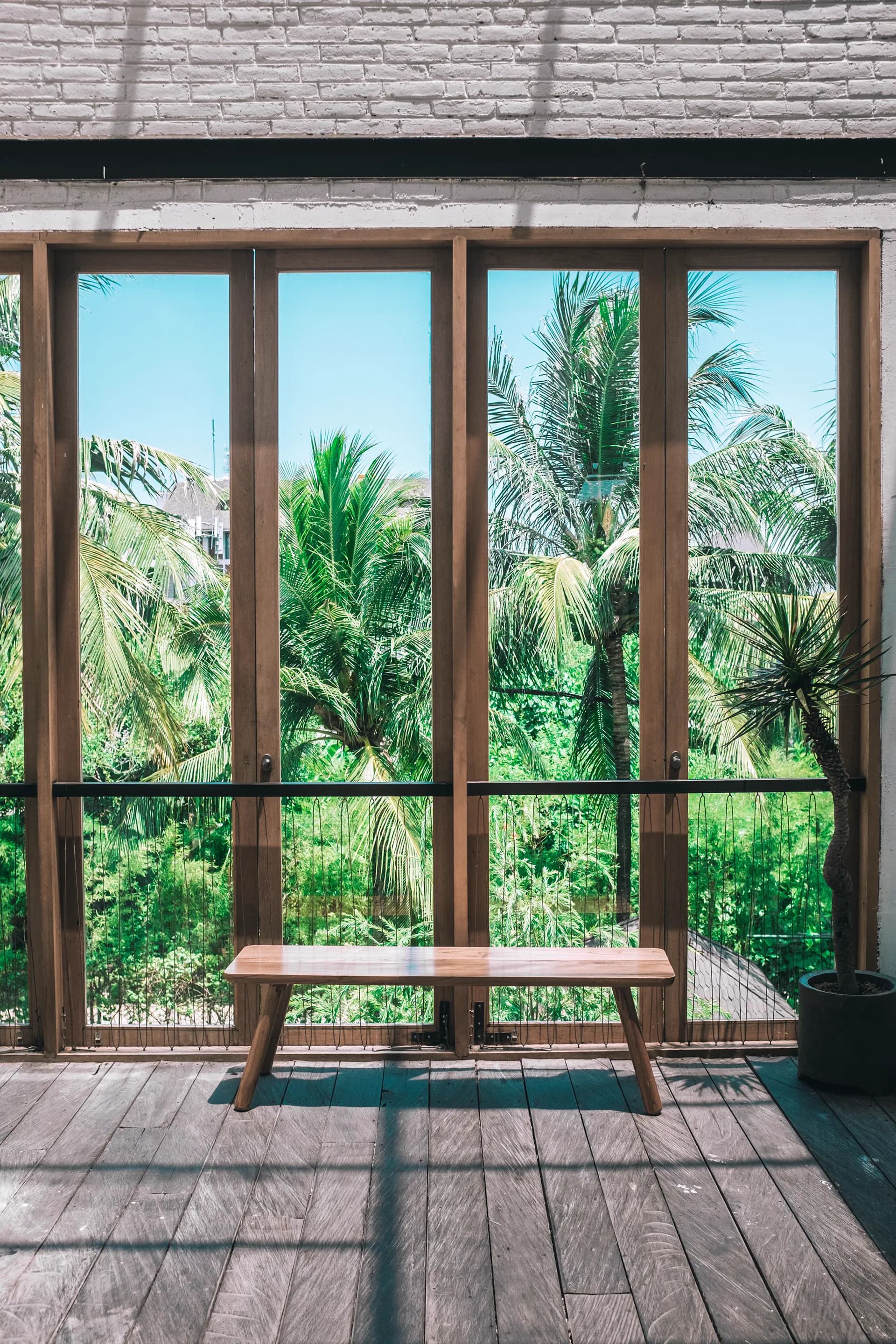Open-air timber-framed verandah with a teak bench looking onto palms