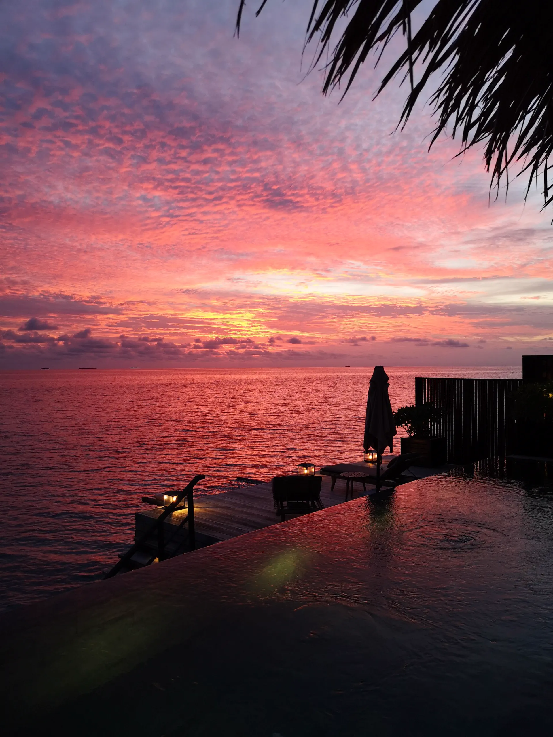 Infinity-edge pool at a tropical resort reflecting a pink and gold sunset sky
